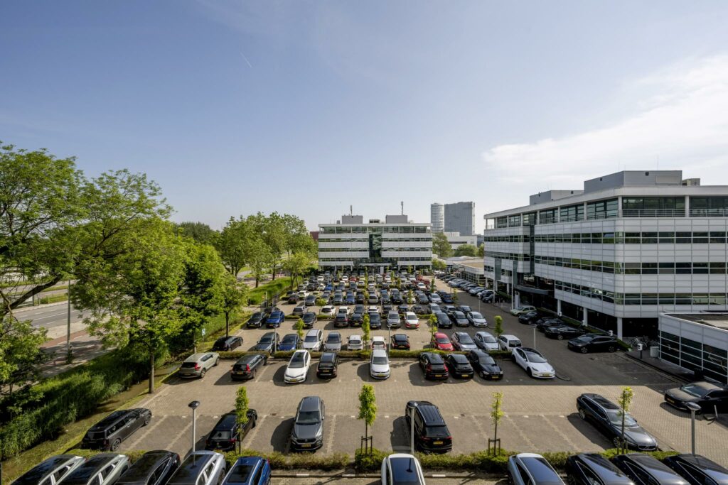 Drukke parkeerplaats tussen moderne kantoorgebouwen aan de Burgemeester Stramanweg in Amsterdam-Zuidoost.